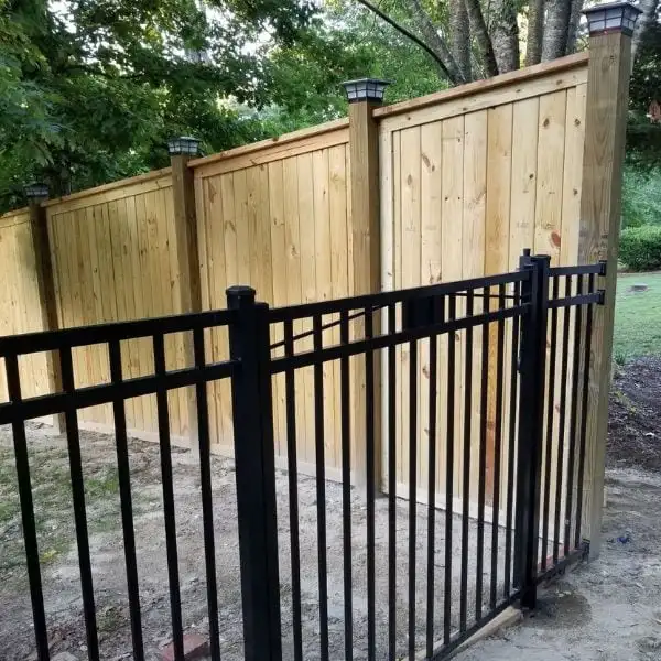 8ft tall picture frame wood fence installed on centered 6x6 posts with a 2x6 cap and solar post lights, connected to a black aluminum fence in Raleigh NC by Innovation’s Fence & Deck