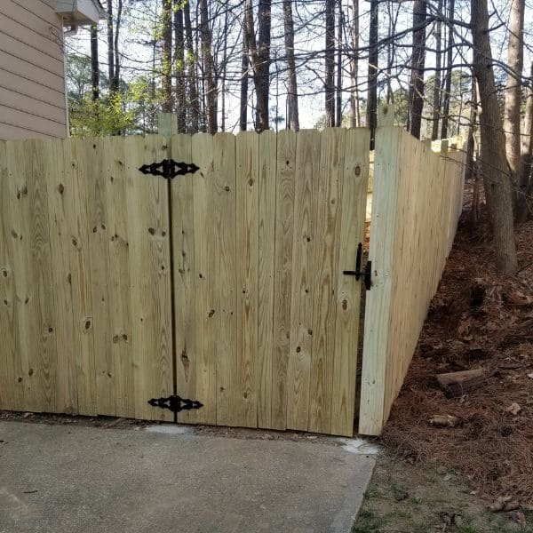 Wood fence installation showing a driveway-end single gate, corner post, short return panel attached to the house, and a long 70‑ft fence run forming an L‑shape in a Cary NC backyard