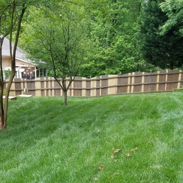 Backyard with green grass and a central tree showing a wood fence where several damaged boards were replaced in Cary NC by Innovation’s Fence & Deck