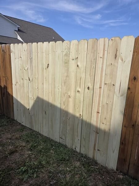 Exterior view of wood privacy fence panel repair showing new boards with stain touch-up in Clayton NC